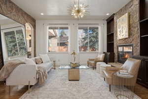 Living area featuring wood finished floors, a stone fireplace, built in features, suspended lighting, and a textured ceiling