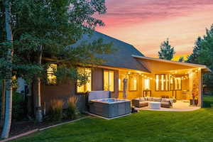 Back of house at dusk with outdoor lounge area, roof with shingles, a lawn, and a patio area
