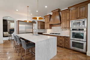 Kitchen featuring wood finish cabinetry, built in appliances, a breakfast bar, pendant lighting, and light stone countertops