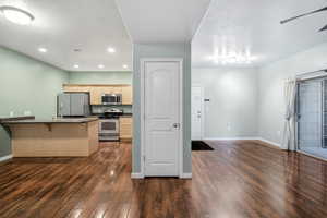 Kitchen featuring a kitchen bar, stainless steel appliances, a peninsula, dark countertops, and dark wood finished floors