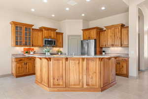 Kitchen with a kitchen breakfast bar, light stone countertops, a large island with sink, wood finish cabinetry, and recessed lighting