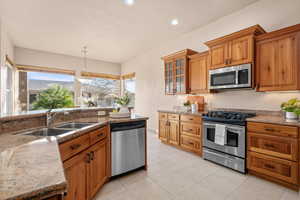 Kitchen featuring stainless steel appliances, glass insert cabinets, wood finish cabinetry, and light stone counters