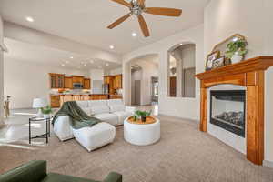 Living area with a tiled fireplace, light colored carpet, a ceiling fan, arched walkways, and recessed lighting
