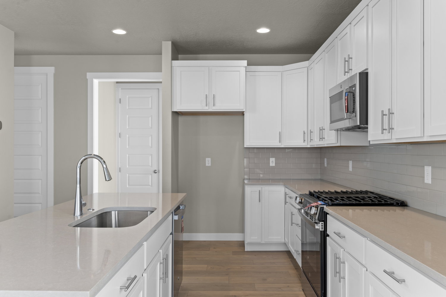 Kitchen featuring stainless steel appliances, a center island with sink, light wood-type flooring, light stone counters, and white cabinets