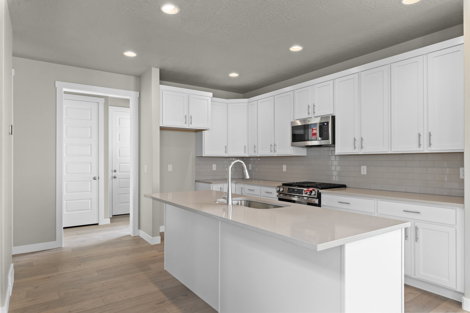 Kitchen featuring a kitchen island with sink, stainless steel appliances, light wood-style floors, white cabinets, and recessed lighting