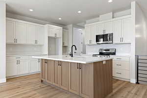 Two tone kitchen with two tone color scheme, an island with sink, light wood-style flooring, stainless steel appliances, and recessed lighting
