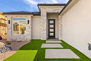 View of exterior entry with stone siding, stucco siding, and a tiled roof