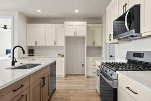 Two tone kitchen featuring stainless steel appliances, light stone countertops, light wood finished floors, recessed lighting, and dual tone cabinetry
