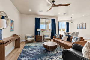 Living area with light wood-style floors, ceiling fan, and a chandelier