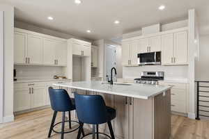 Two tone kitchen with an island with sink, stainless steel appliances, a breakfast bar area, light wood-style floors, and recessed lighting