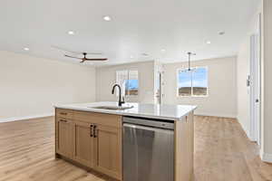 Kitchen featuring stainless steel dishwasher, light wood-style flooring, light stone countertops, and a kitchen island with sink