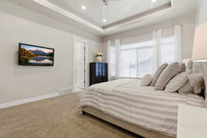 Carpeted bedroom with a tray ceiling, a ceiling fan, recessed lighting, and crown molding