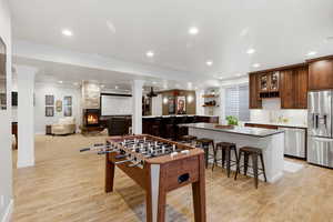 Game room featuring light wood-style floors, ornate columns, a stone fireplace, recessed lighting, and bar with sink