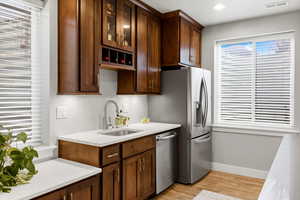 Kitchen with glass fronted cabinets, stainless steel appliances, light stone countertops, light wood finished floors, and dark wood finish cabinetry