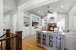 Living area featuring light wood finished floors, a tile fireplace, vaulted ceiling, a ceiling fan, and built in features