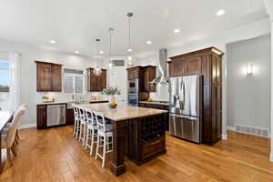 Kitchen featuring dark wood finish cabinets, stainless steel appliances, light stone countertops, and a kitchen bar