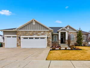Craftsman-style home featuring board and batten siding, a garage, concrete driveway, and stone siding