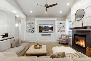 Carpeted living room featuring lofted ceiling, built in shelves, ceiling fan, a fireplace, and recessed lighting