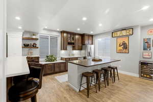 Two tone kitchen featuring a kitchen breakfast bar, two tone cabinetry, wine cooler, light wood-type flooring, and recessed lighting