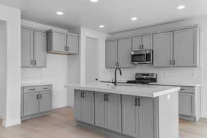 Kitchen with gray cabinetry, tasteful backsplash, stainless steel appliances, light wood-type flooring, and recessed lighting