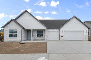 View of front facade with board and batten siding, covered porch, a garage, and stone siding