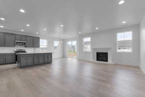 Kitchen with open floor plan, light countertops, a center island with sink, a glass covered fireplace, and gray cabinets