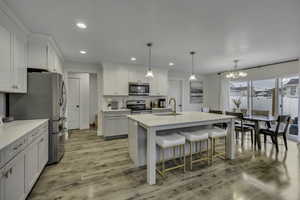 Kitchen featuring a breakfast bar, an island with sink, stainless steel appliances, light wood-style floors, and a chandelier