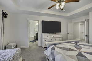 Bedroom with a raised ceiling, light colored carpet, a ceiling fan, and connected bathroom