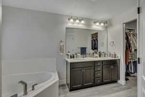 Bathroom featuring double vanity, a bath, light wood finished floors, and a spacious closet