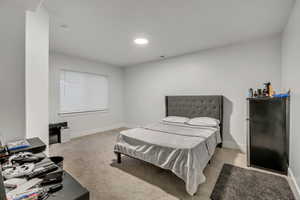 Bedroom with light colored carpet and freestanding refrigerator