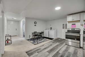 Kitchen featuring stainless steel electric range, white cabinetry, washing machine and clothes dryer, and light countertops