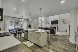 Kitchen featuring open floor plan, light wood finished floors, an island with sink, and a warm lit fireplace