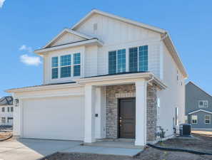 View of front facade featuring stone siding, a garage, concrete driveway, and board and batten siding