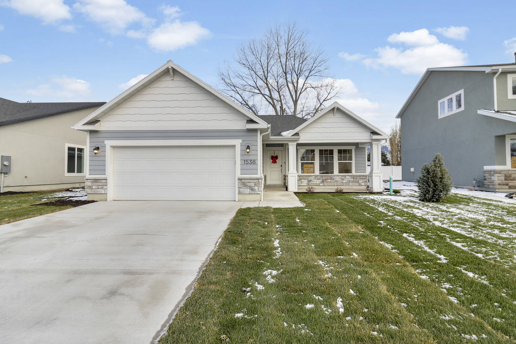 View of front of house with a garage, stone siding, driveway, a front lawn, and covered porch