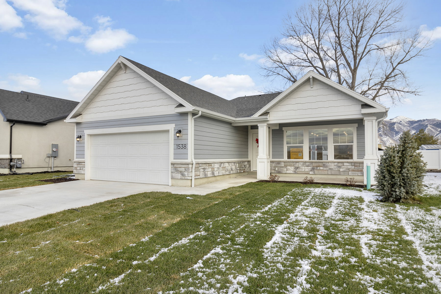 Single story home featuring stone siding, an attached garage, a lawn, driveway, and roof with shingles