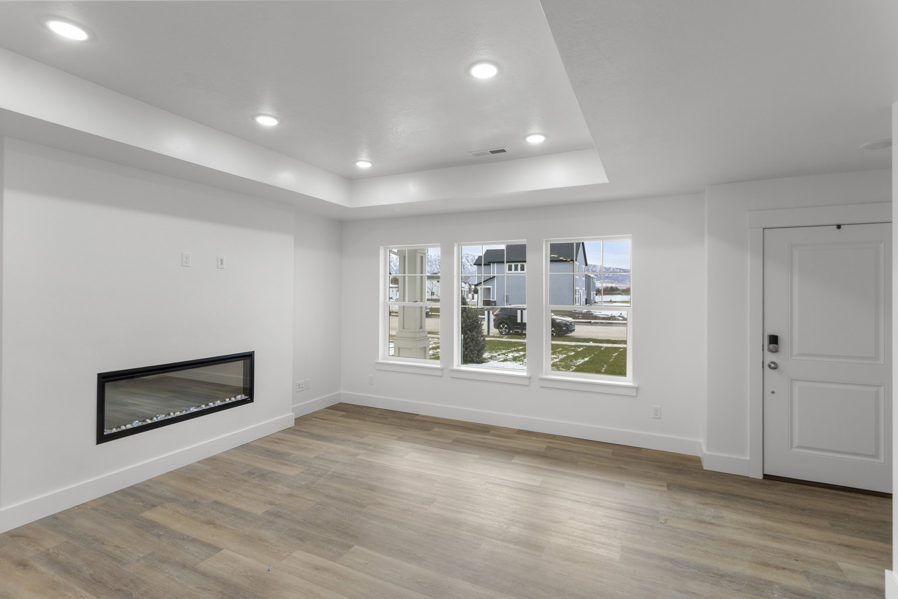 Unfurnished living room featuring a tray ceiling, a glass covered fireplace, light wood finished floors, and recessed lighting