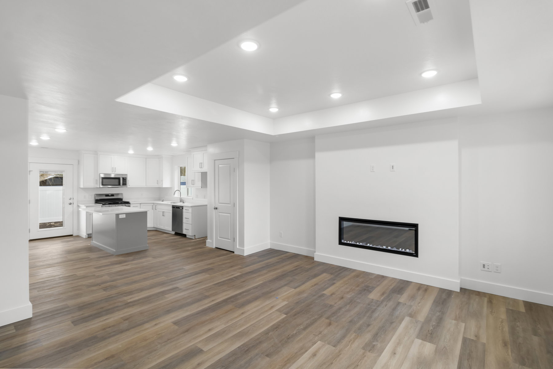Unfurnished living room featuring recessed lighting, a glass covered fireplace, dark wood finished floors, and a raised ceiling