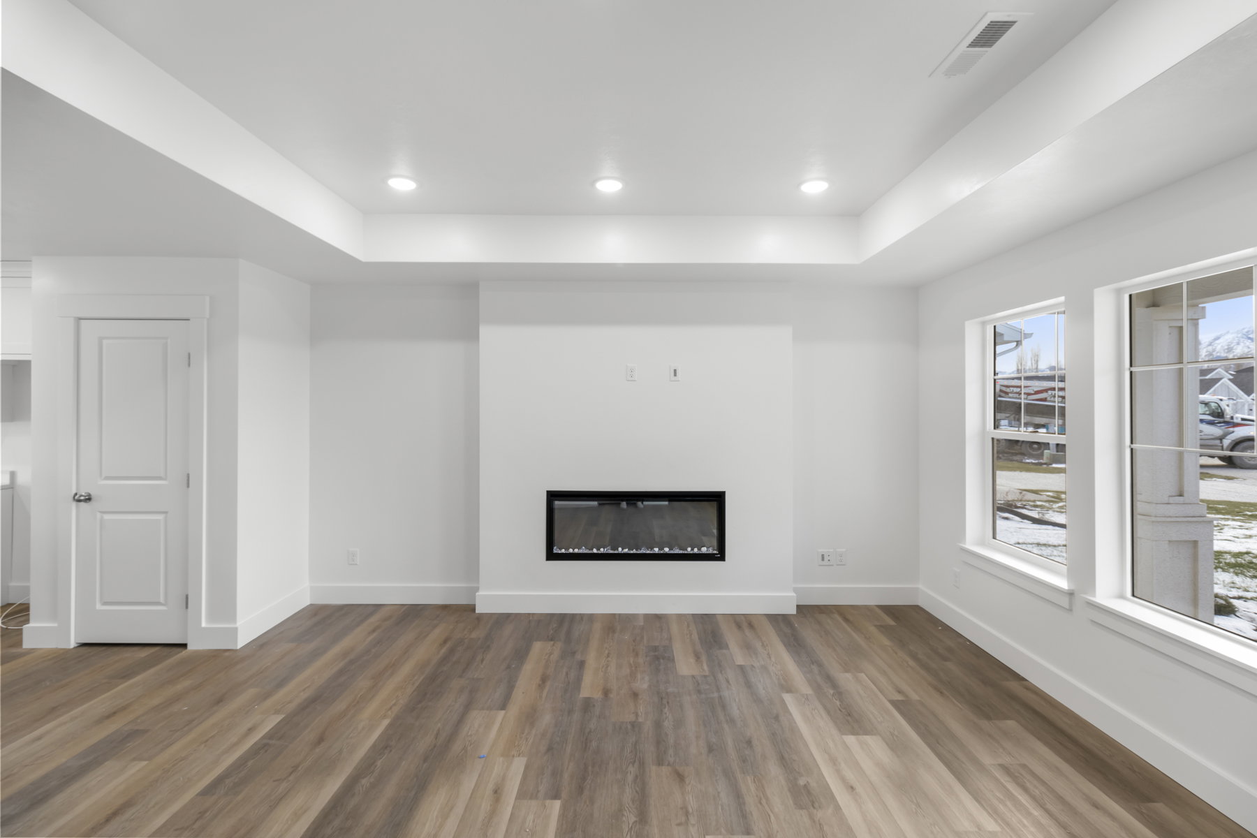 Unfurnished living room with a tray ceiling, a glass covered fireplace, wood finished floors, and recessed lighting