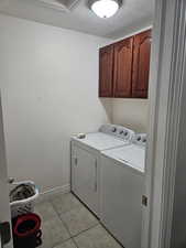 Laundry room featuring cabinet space, a textured ceiling, separate washer and dryer, and light tile patterned floors