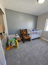 Carpeted bedroom with a nursery area and a textured ceiling