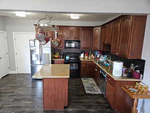 Kitchen featuring black and stainless steel appliances, a kitchen island, tasteful backsplash, and dark wood-style floors