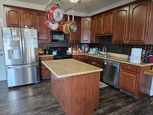 Kitchen with appliances, light countertops, dark wood-style floors, and a kitchen island