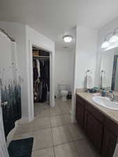 Primary Bathroom featuring curtained shower, vanity, a textured ceiling, light tile patterned floors, and a spacious closet
