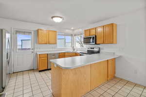 Kitchen with a peninsula, light tile patterned flooring, light countertops, stainless steel appliances, and plenty of natural light
