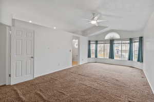 Spacious primary bedroom with vaulted ceilings, large bay windows, and ceiling fan