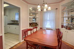 Dining room featuring hanging lights, light wood-style floors, built in shelves, and ornamental molding