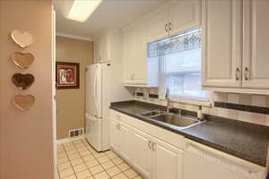 Kitchen featuring white cabinets, white appliances, dark countertops, light tile patterned flooring, and ornamental molding