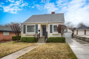 View of front of house with a front lawn, a chimney, roof with shingles, a garage, and an outbuilding