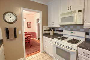 Kitchen featuring dark countertops, white appliances, and decorative backsplash