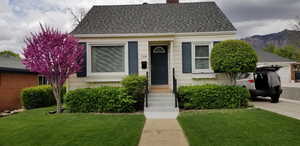 View of front facade featuring a front lawn, roof with shingles, a chimney, and entry steps